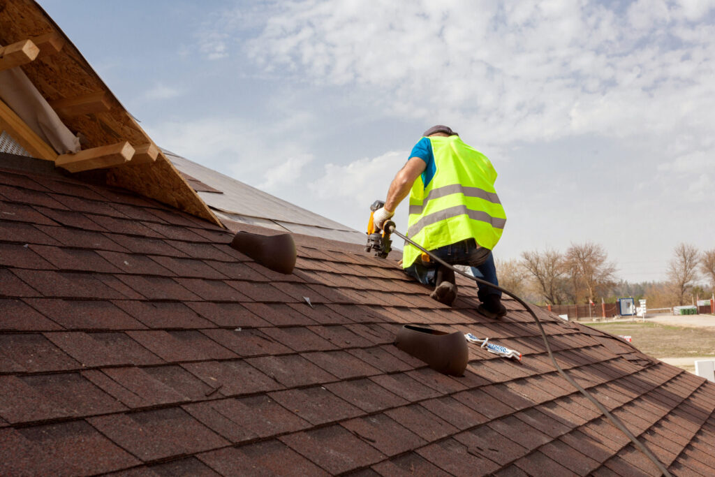 Man with a drill installing shingles on a roof