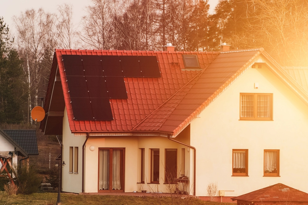 Stucco house with clay roofing, roof solar panels, and a lens flair