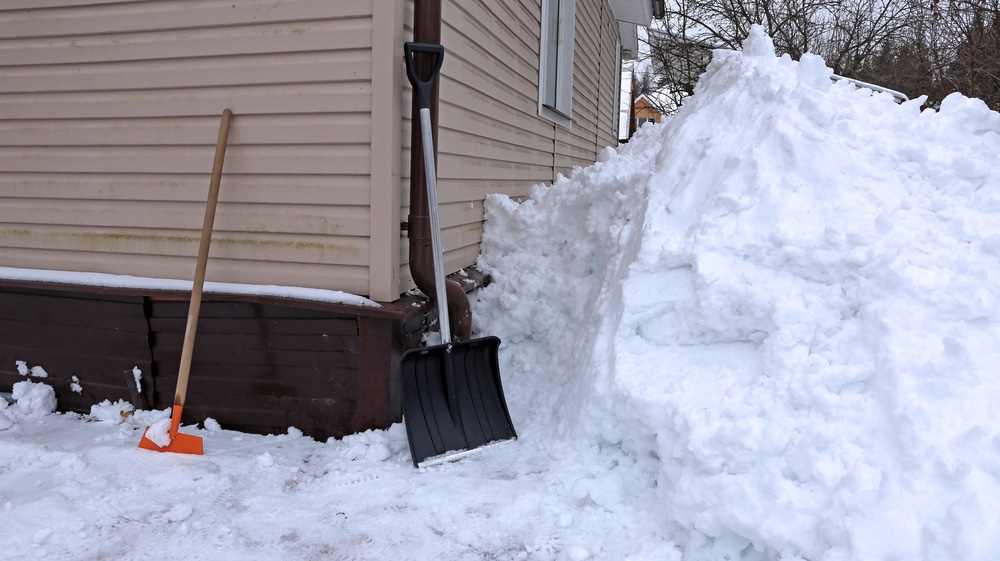 Shovels on the side of a house next to snow